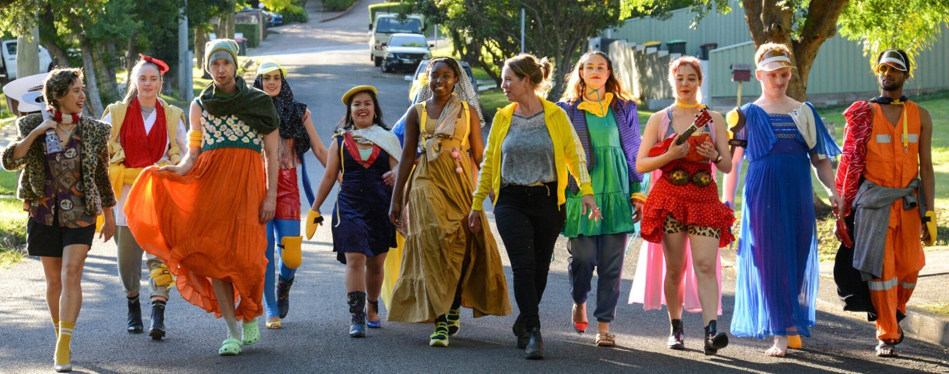 Dancers in bright costumes walking through a leafy street